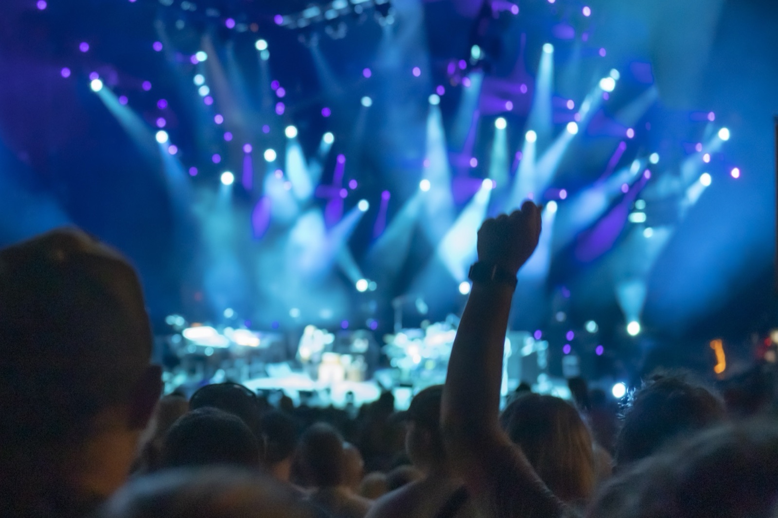 A fan raises a fist in front of a blurred stage washed in blue and violet spotlight beams.