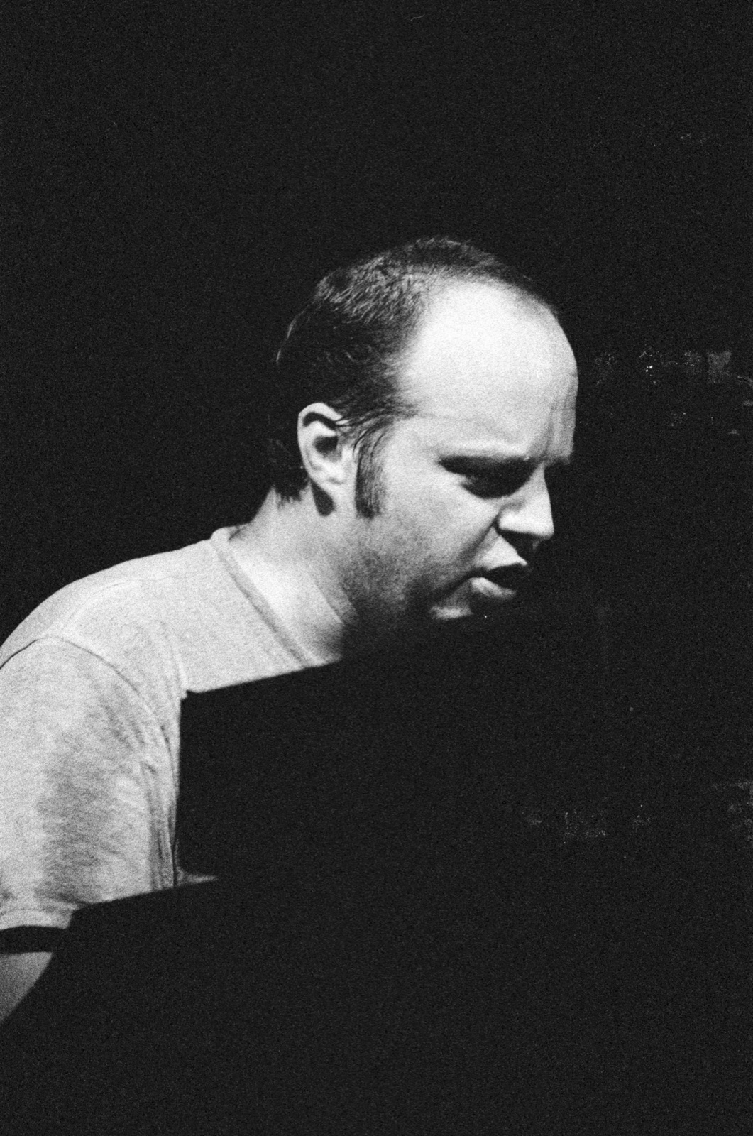 In black and white, the organist leans over his keys with his eyes down against a black background.